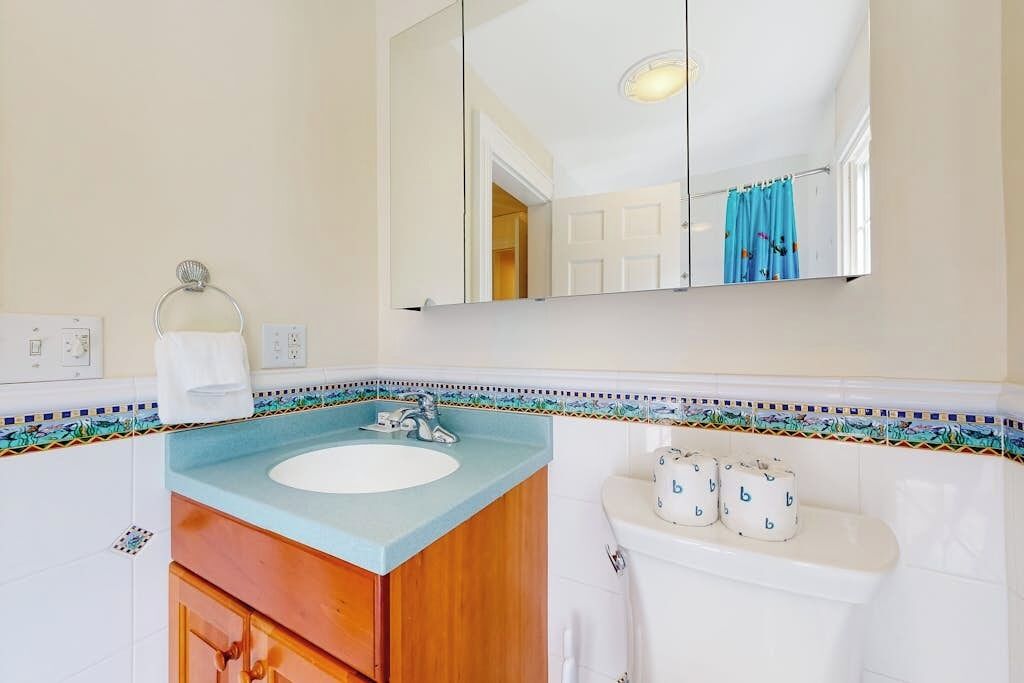 A bathroom with a sink, mirror, toilet, and decorative tiles.
