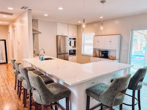A modern kitchen with a large island, bar stools, stainless steel appliances, and pendant lighting. - Pool - Fire Pit - Game Room - Close to Downtown - Hammock (St. Augustine)