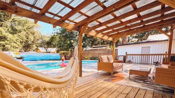 Um deck de madeira com uma rede, móveis de vime e uma piscina.