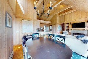 A wooden interior with a dining table, chairs, a sofa, a television, and a fireplace.