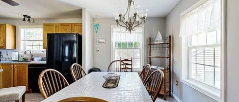 A kitchen with a dining table, chairs, a chandelier, and a refrigerator.