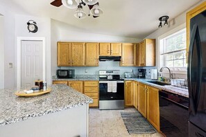 Una cocina con encimeras de granito, armarios de madera, horno de acero inoxidable, microondas y refrigerador.