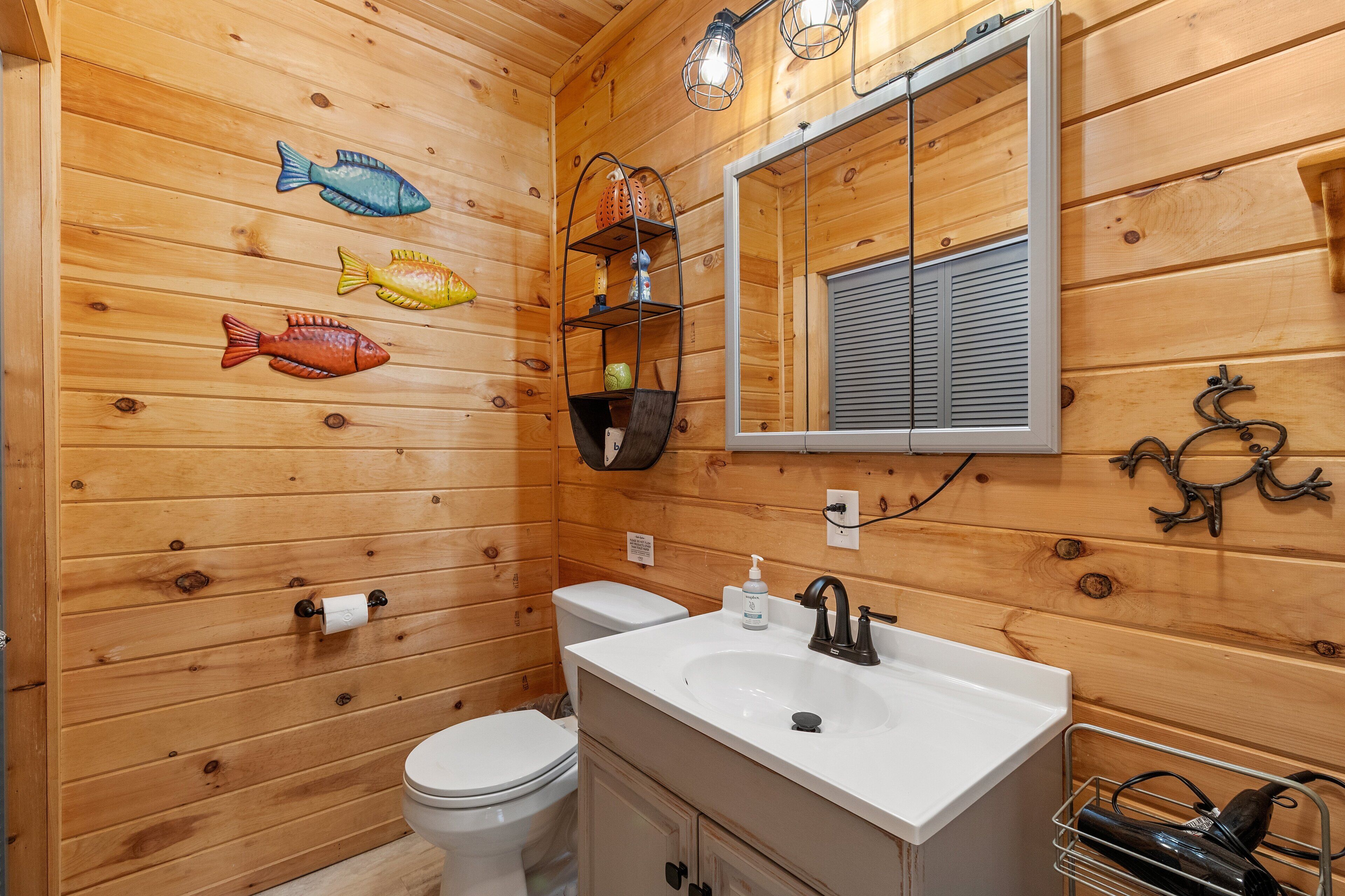 A wooden-paneled bathroom with a toilet, sink, and decorative fish wall art.