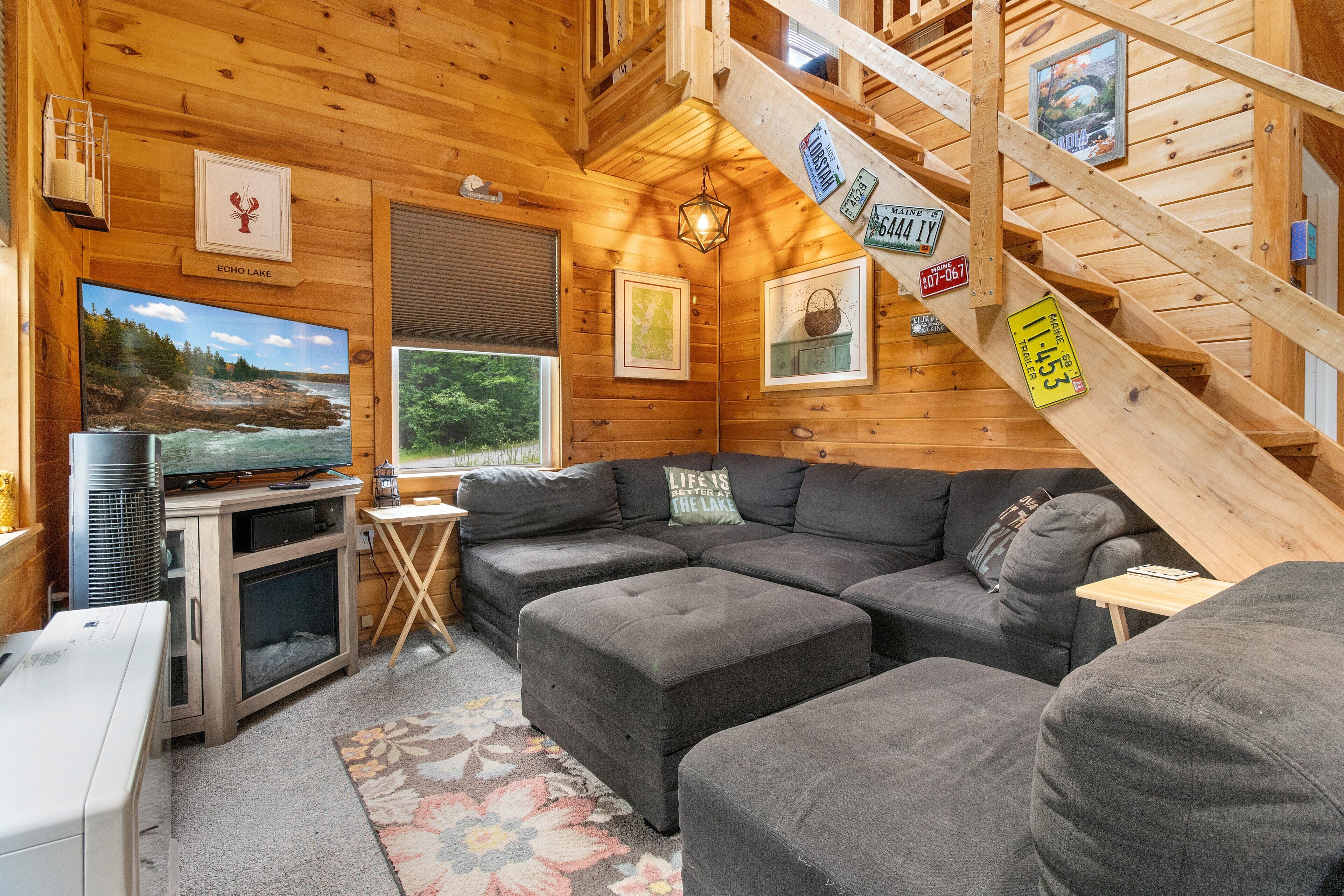 Interior de cabana de madeira com sofá em seção, televisão de tela plana, lareira e escada.