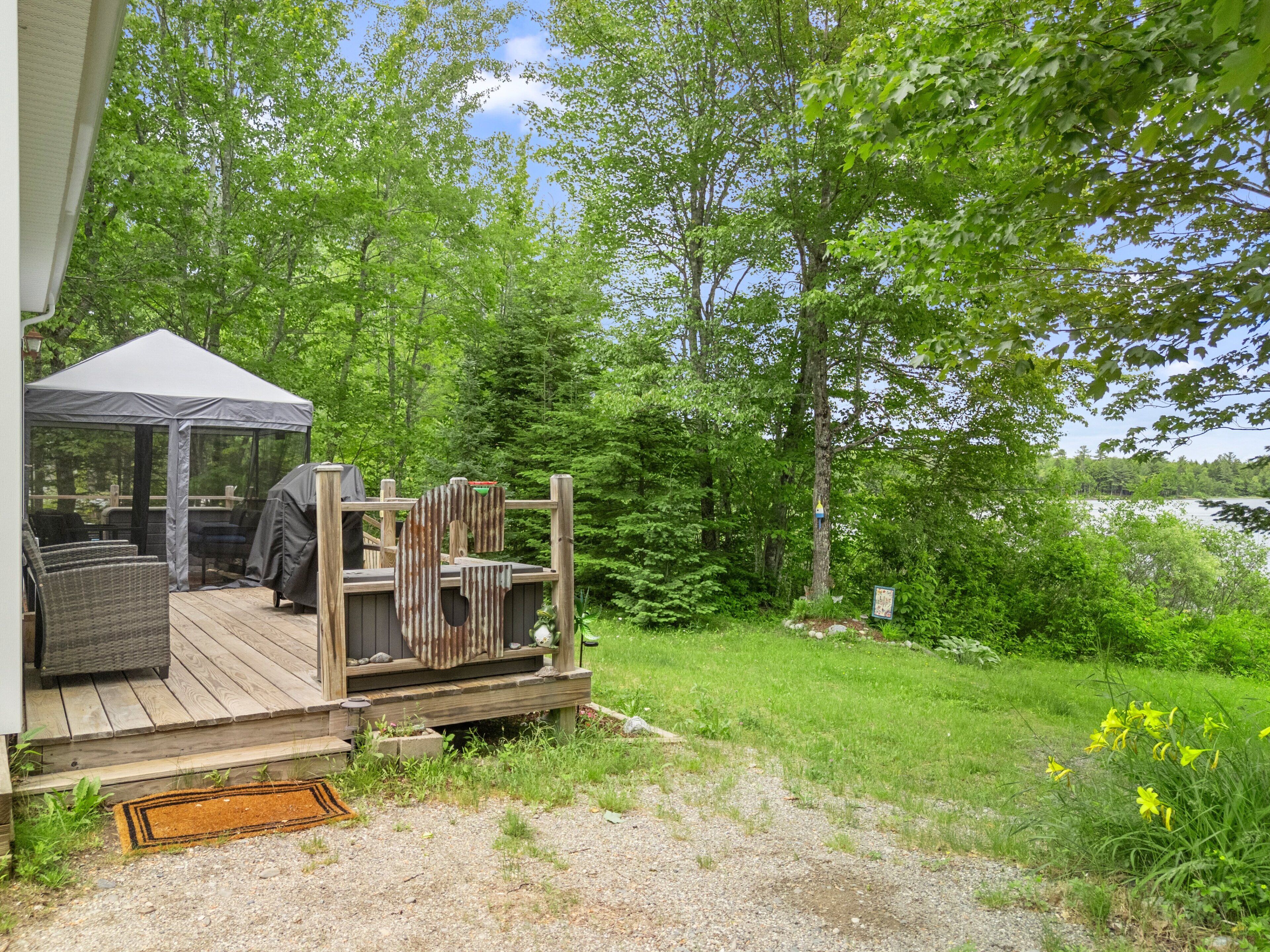 A wooden deck with outdoor furniture, a covered seating area, and a view of a lake surrounded by trees.