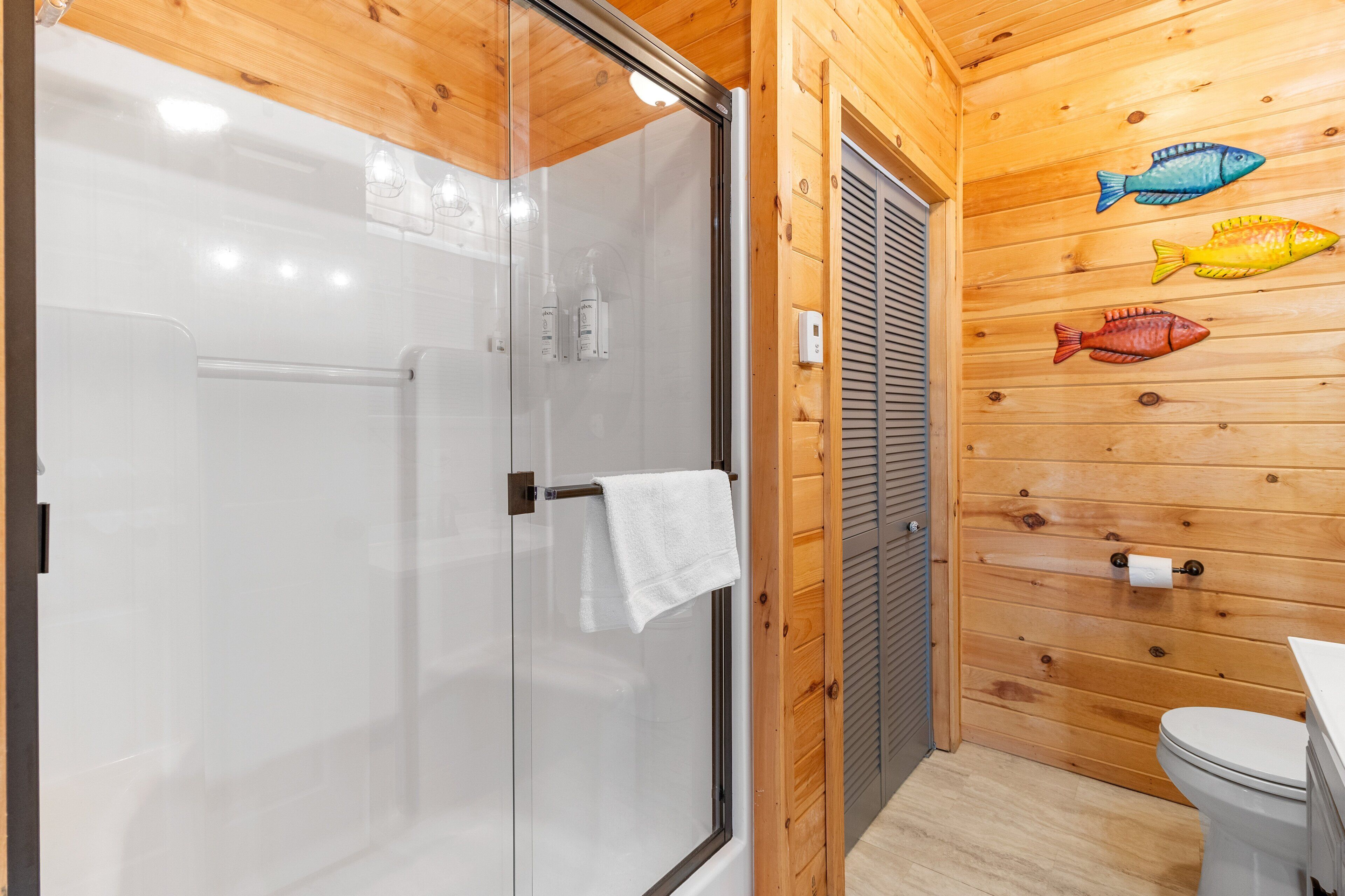 A wooden interior with a glass shower door, a toilet, and a towel hanging on the door.
