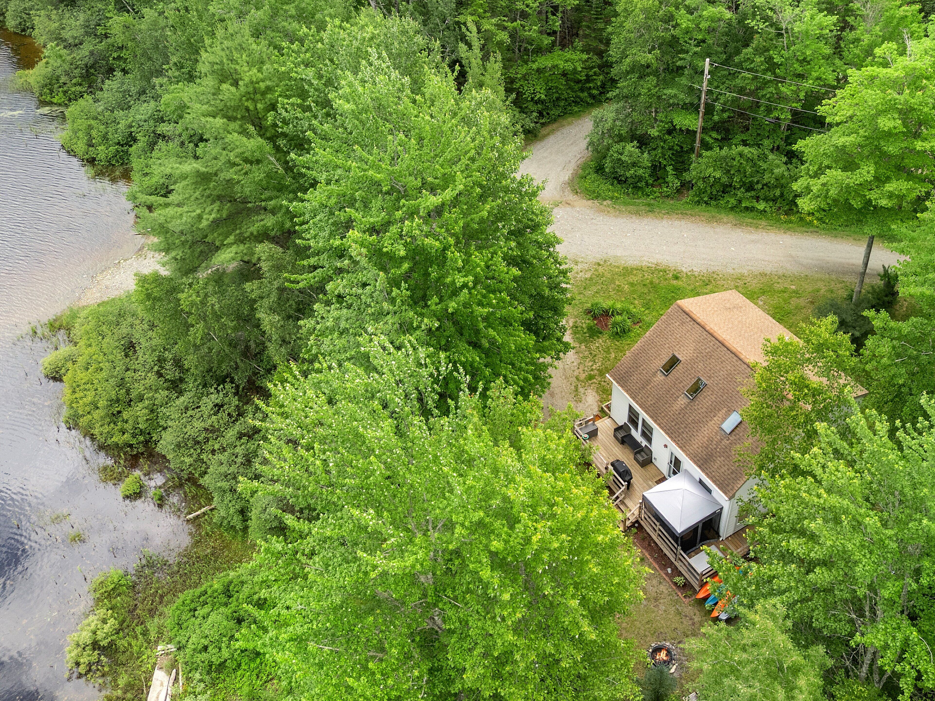 A house with a deck, surrounded by dense greenery and a river.