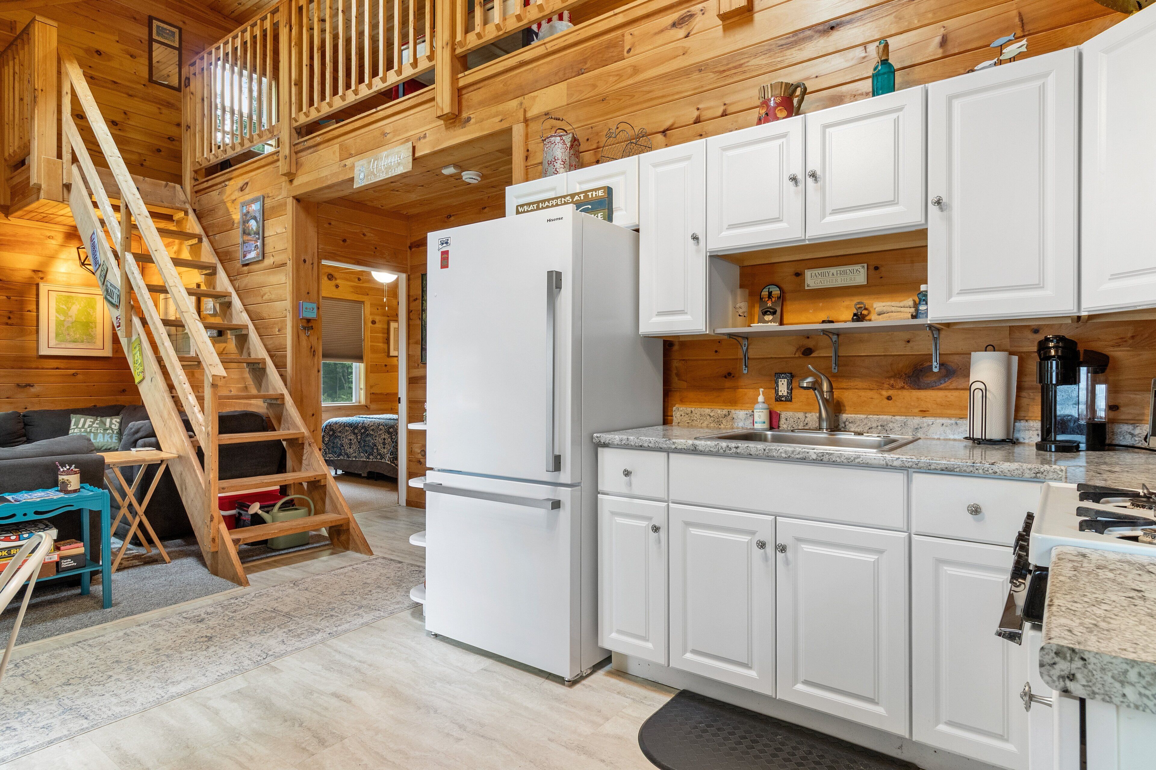 A wooden cabin interior with a kitchen, a dining area, and a staircase.