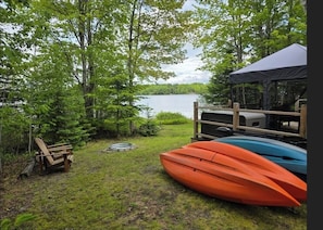 A lakeside cabin with kayaks, a deck chair, and a tent.