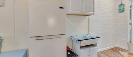 Een praktische keuken met witte kastjes, een koelkast, een klein aanrecht en een prullenbak.
