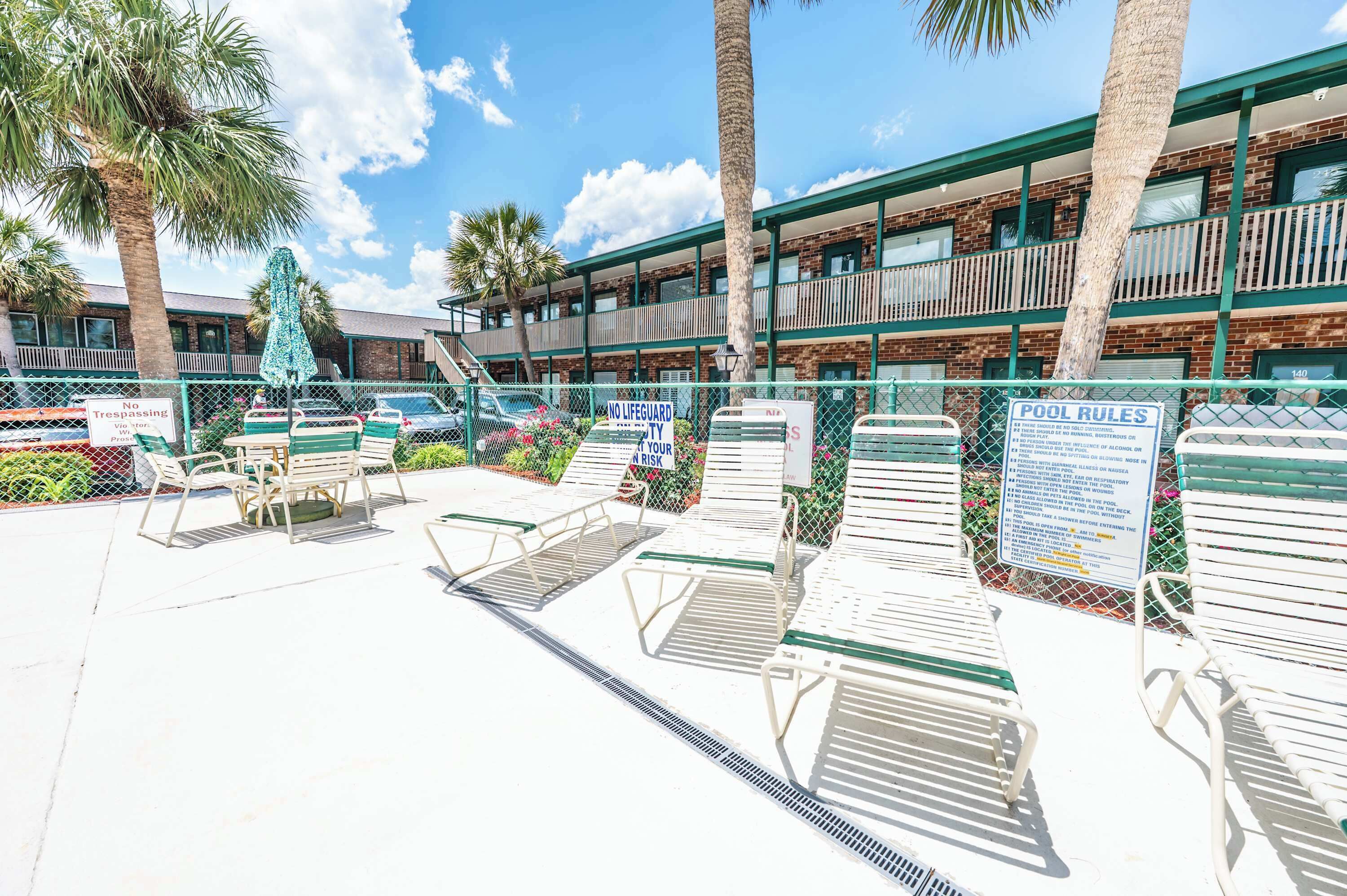 A pool area with lounge chairs, palm trees, and a building with multiple balconies.