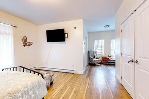 Ein Schlafzimmer mit Bett, einem an der Wand befestigten Fernseher, einem Sessel und einer Tür.