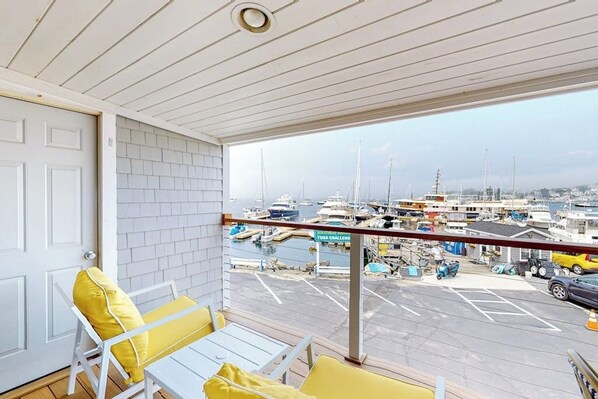 A balcony with white railings, yellow cushions, and a view of a marina with boats. - Oceanfront, dog-friendly condo with Boothbay Harbor views & prime location (Boothbay Harbor)