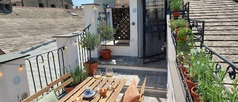 A rooftop terrace with a wooden table and chairs, potted plants, and a small seating area.