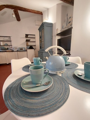 A dining area with a white table set with blue tableware, a vintage kettle, and a cabinet with decorative items. - "Acquamarina House" The terrace in the heart of downtown Genoa (Genova)