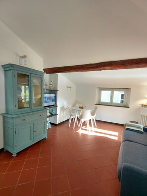 Ein Wohnzimmer mit einem blauen Schrank, weißen Stühlen, einem Esstisch und einem Fenster.