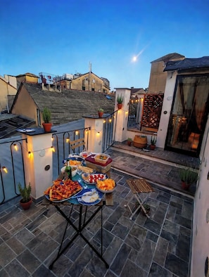 Un patio al aire libre con una mesa lista para comer, rodeado de macetas con plantas y una guirnalda de luces.