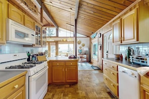A kitchen with wooden cabinets, a central island, and a view to the dining area. - Stunning artist's retreat with ocean view & amazing deck, near Reid State Park (Georgetown)