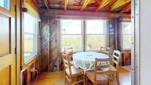 A wooden dining room with a round table and six chairs, large windows, and a view of the outdoors. - Charming abode with water views, updated kitchen, & internet - dog-friendly (Castine)