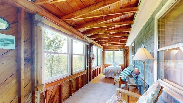 A wooden interior with a high ceiling, large windows, a bed, a chair, and a lamp. - Charming abode with water views, updated kitchen, & internet - dog-friendly (Castine)