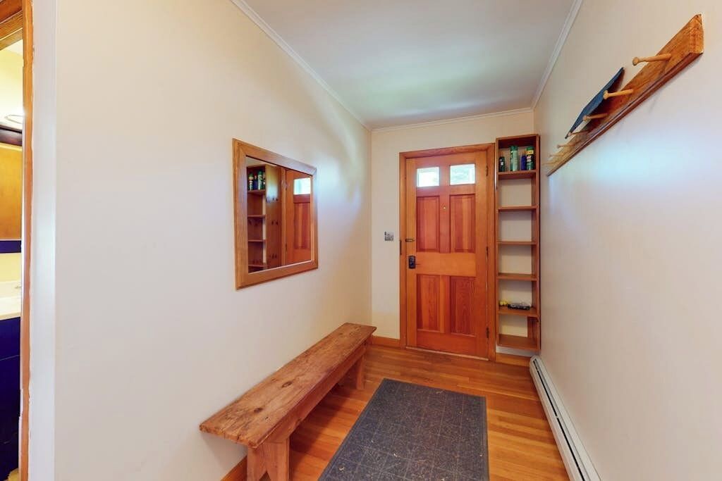 A hallway with a wooden bench, a door with a mirror, and a shelf with bottles.