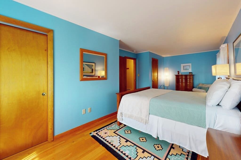 A bedroom with a bed, a wooden door, a mirror, and a rug.