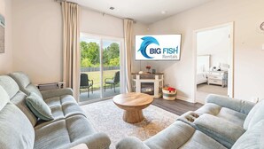 Una sala de estar moderna con un sofá, una mesa de centro y una pantalla de televisión que muestra 'BIG FISH Rentals'.