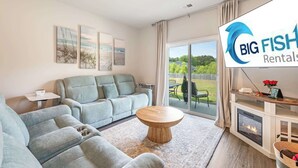 Una sala de estar moderna con sofá, una mesita de centro y chimenea. Hay un ventanal con vistas al exterior.