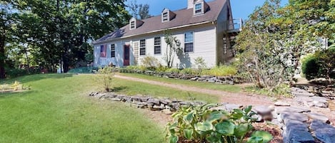 A two-story house with a stone pathway leading to the front door, surrounded by a well-maintained lawn and various shrubs.