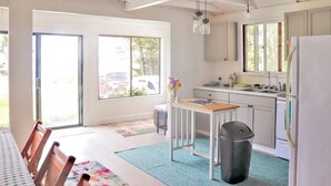Una cocina con una mesa de comedor, sillas, un cesto de basura y una ventana.