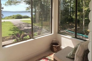 Ein Zimmer mit großen Fenstern und Blick auf eine Wiese und Bäume.