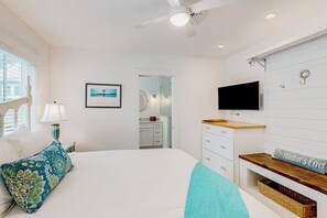 Ein Schlafzimmer mit einem Bett, einem Fernseher, einem Deckenventilator, einem Fenster und einer Tür zu einem Badezimmer.