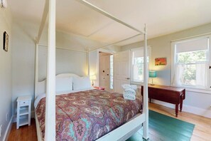Een hemelbed met een gebedene, een nachtkastje, een bankje en een raam met gordijnen.