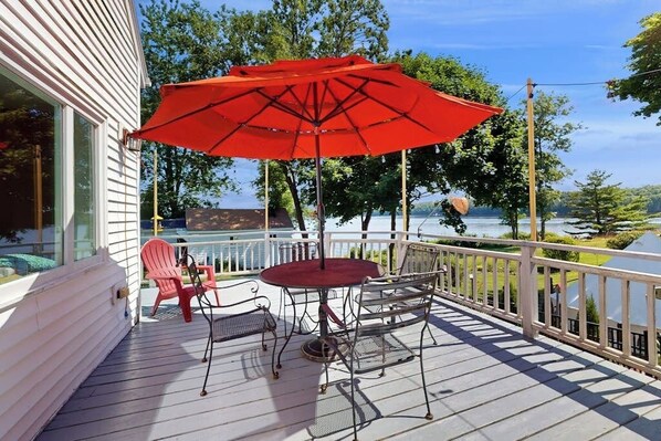 Une terrasse avec une table et des chaises, un parasol rouge et une vue sur un lac.