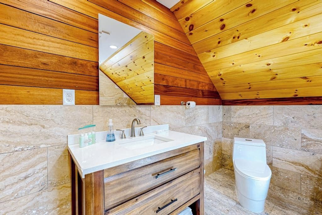 A bathroom with a wooden ceiling, a sink with a marble countertop, and a toilet.