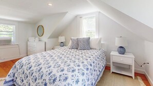 Un dormitorio con una cama grande, una mesita de noche con lámpara, un aparador y una ventana.