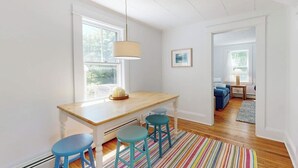Una habitación luminosa con una mesa de madera, taburetes azules, un tapete a rayas y una lámpara colgante.