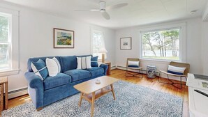 Un salón espacioso con un sofá azul, una mesa de centro de madera y un ventilador de techo.