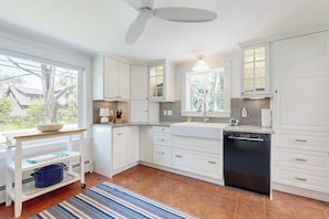 Una cocina moderna con armarios blancos, un lavavajillas negro y una ventana con vistas a un jardín.