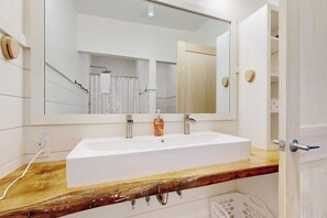 A bathroom with a white sink, wooden countertop, and a large mirror.