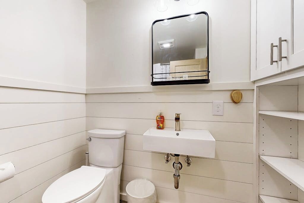 A bathroom with a toilet, sink, mirror, and storage cabinets.