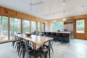 A modern kitchen with a dining area, large windows, and a ceiling fan.