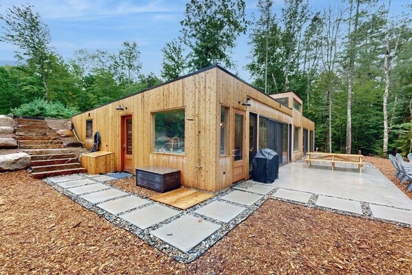 A wooden cabin with a glass door, a small porch, and a concrete patio. - Idyllic lakeside house with outdoor sauna, patio and firepit (Hope)