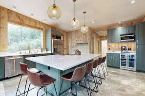 A modern kitchen with a large island, bar stools, and wooden paneling. - Idyllic lakeside house with outdoor sauna, patio and firepit (Hope)