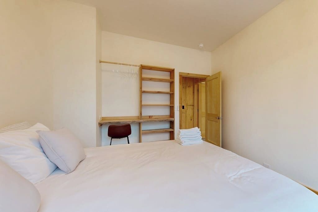 A bedroom with a bed, a wooden wardrobe, a chair, and a door.