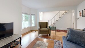 A living room with a television, a sofa, a chair, and a staircase. - Charming Camden Retreat with Front Porch, Deck and Wifi (Camden)