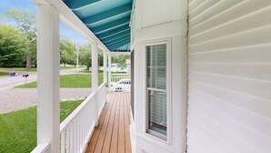A covered porch with white siding, a wooden deck, and a view of a street with a mailbox and a mailbox post. - Charming Camden Retreat with Front Porch, Deck and Wifi (Camden)