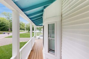 A covered porch with white siding, a wooden deck, and a view of a street with a mailbox and a mailbox post.