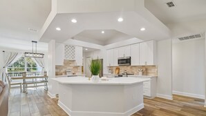 Een moderne keuken met een groot eiland, witte kasten en uitzicht op buiten.
