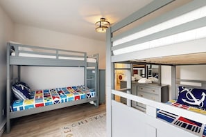 Ein Schlafraum mit Etagenbetten und maritimen Dekor, darunter ein Bett mit farbenfroher Steppdecke und einem Kissen mit Anker-Motiv.